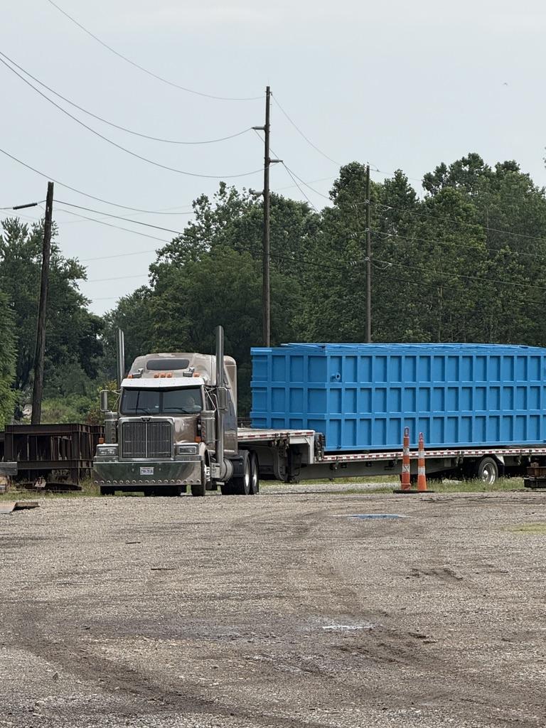 Semi truck hauling a blue EnviroBox tank on a flatbed trailer