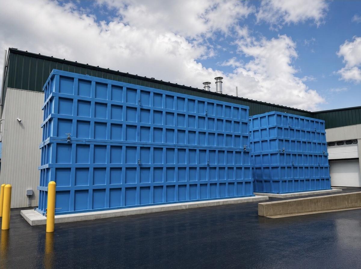 Two pairs of blue EnviroBox tanks stacked two-high on concrete pads beside an industrial building