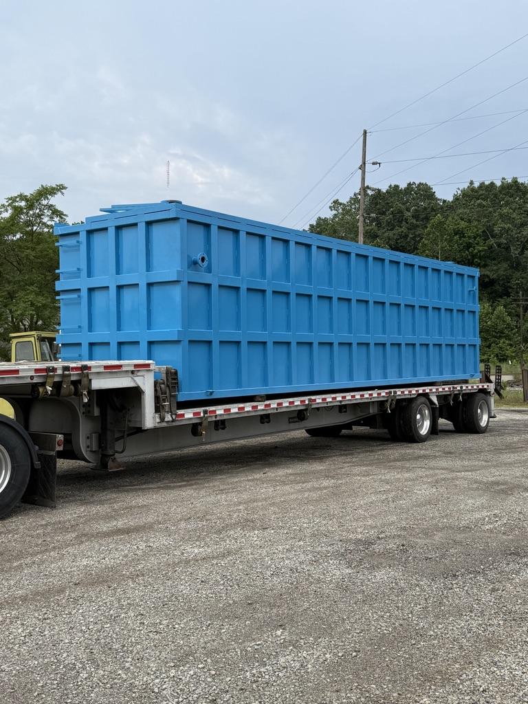 Blue EnviroBox tank staged on a flatbed trailer in the yard