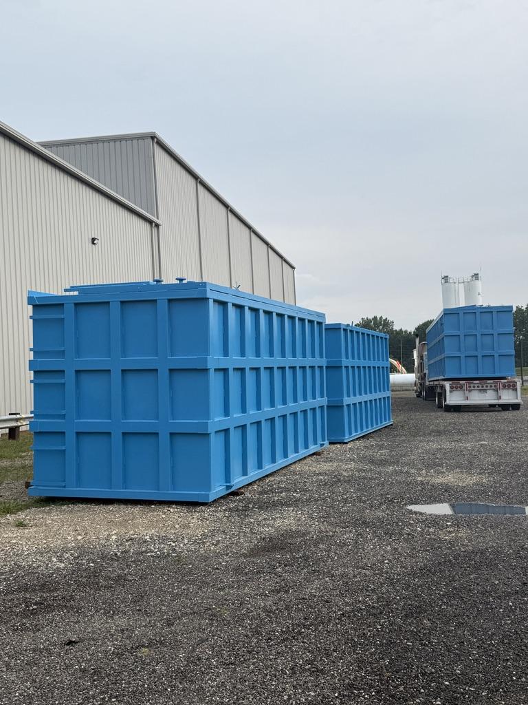 Multiple coated blue EnviroBox tanks staged outside the shop with a delivery trailer